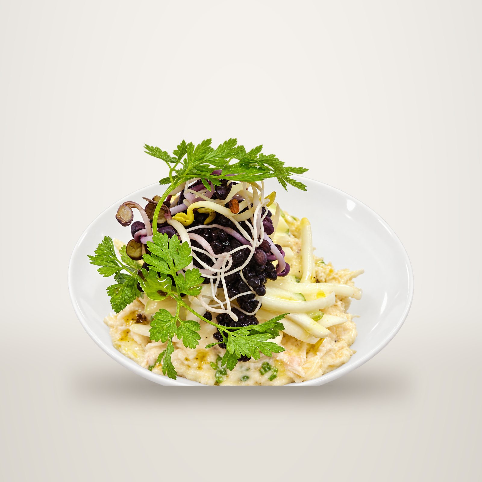 Gros plan sur une assiette blanche de chair de crabe avec des bâtonnets de céleri, du caviar noir, des pousses germées et du cerfeuil.