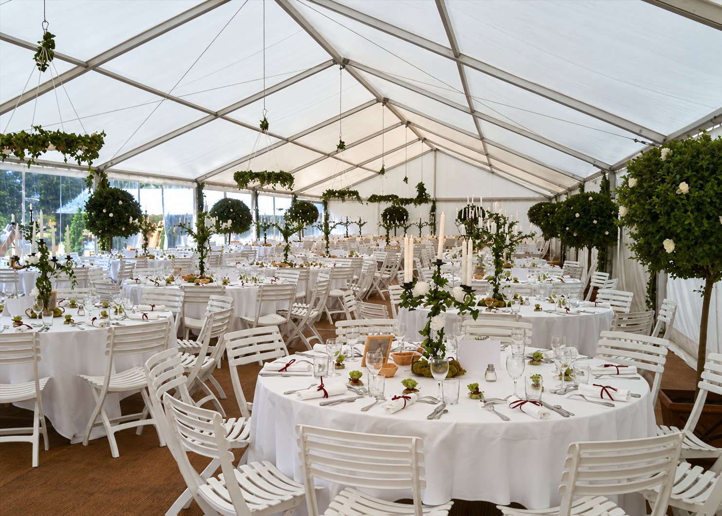 Intérieur d'une grande tente blanche aménagée pour une réception, avec des tables rondes nappées de blanc, des chaises blanches et des décorations végétales.